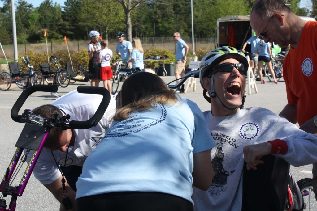 A man sitting on a handcycle has large smile on his face after he finished his bike ride.