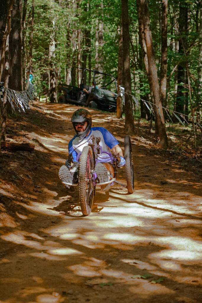 A man rides an off-road handcycle down a dirt trail.