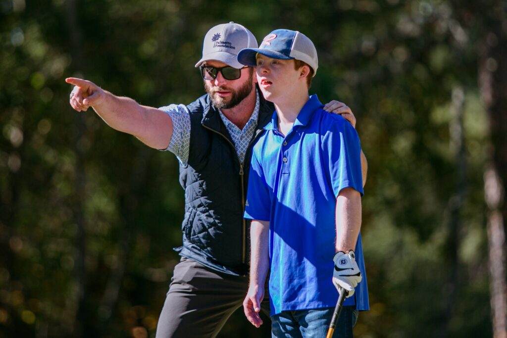 A golf coach points in the direction that a young golfer should hit the ball.
