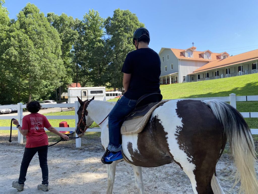 A young man rides a brown and white horse while a woman holds the lead line.