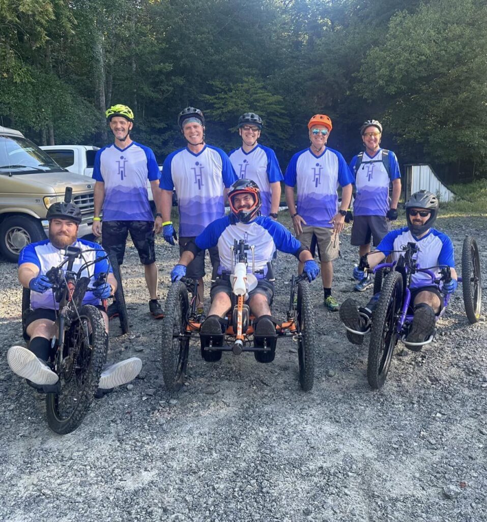 Heather's Ride Mountain Bike Team poses for a photo with 3 adaptive mountain bikers in the front and 5 support riders behind them,.