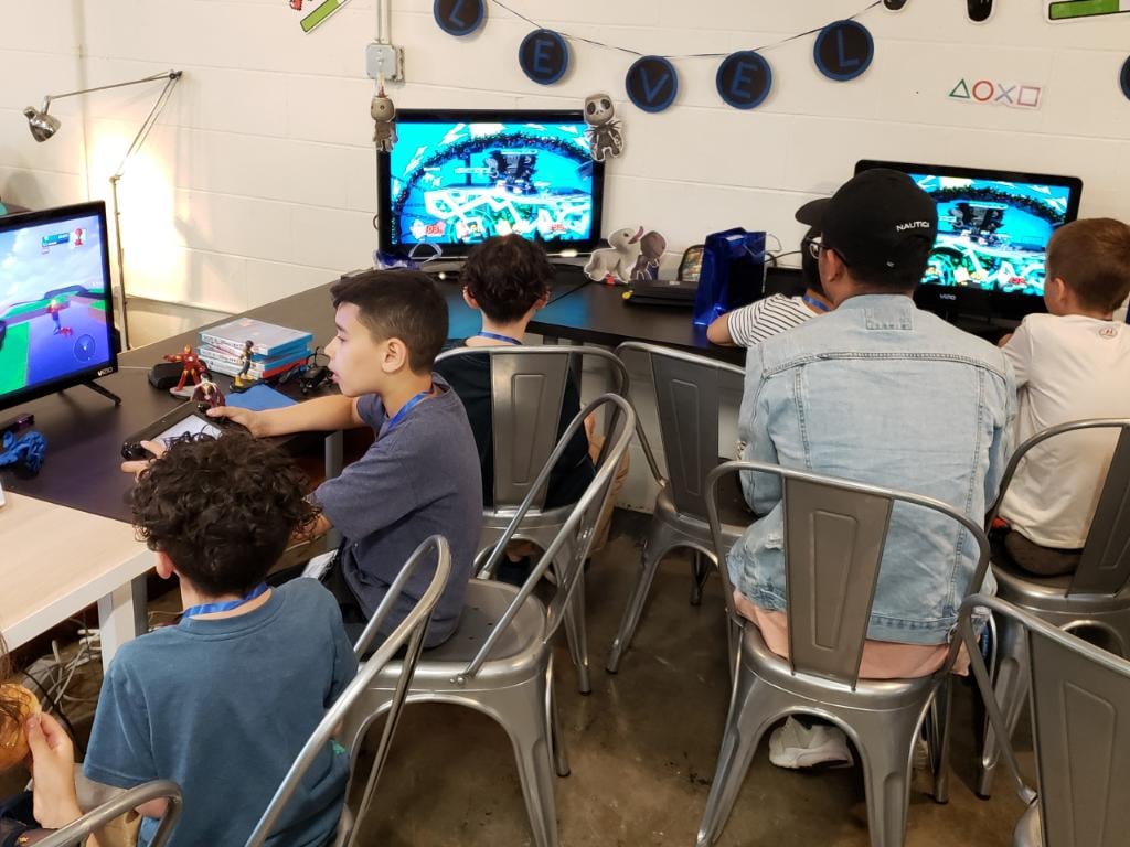 4 boys sit around three different screens playing video games.