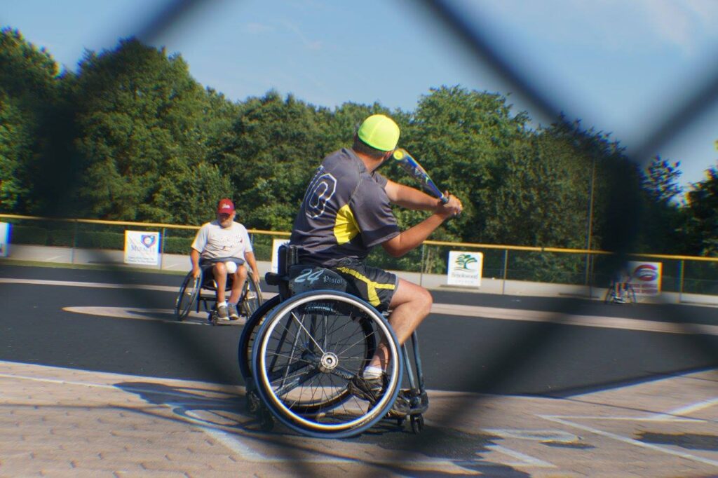 A baseball player who uses a wheelchair swings at the ball in a game.