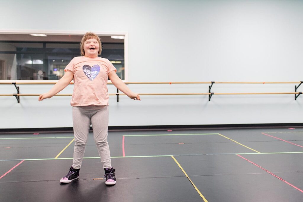  A young woman dances with a large smile on her face in a dance studio.
