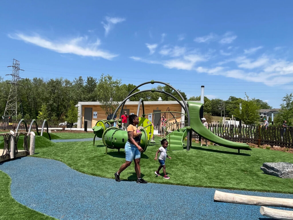 A woman and child walk through a playground with lots of play features.
