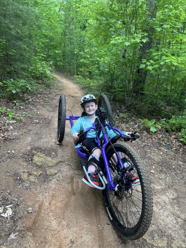 A young man rides a handcycle down a trail.