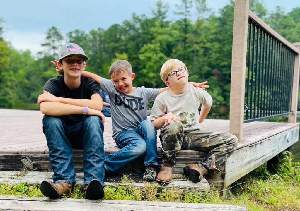 3 young boys sit next to each other smiling.