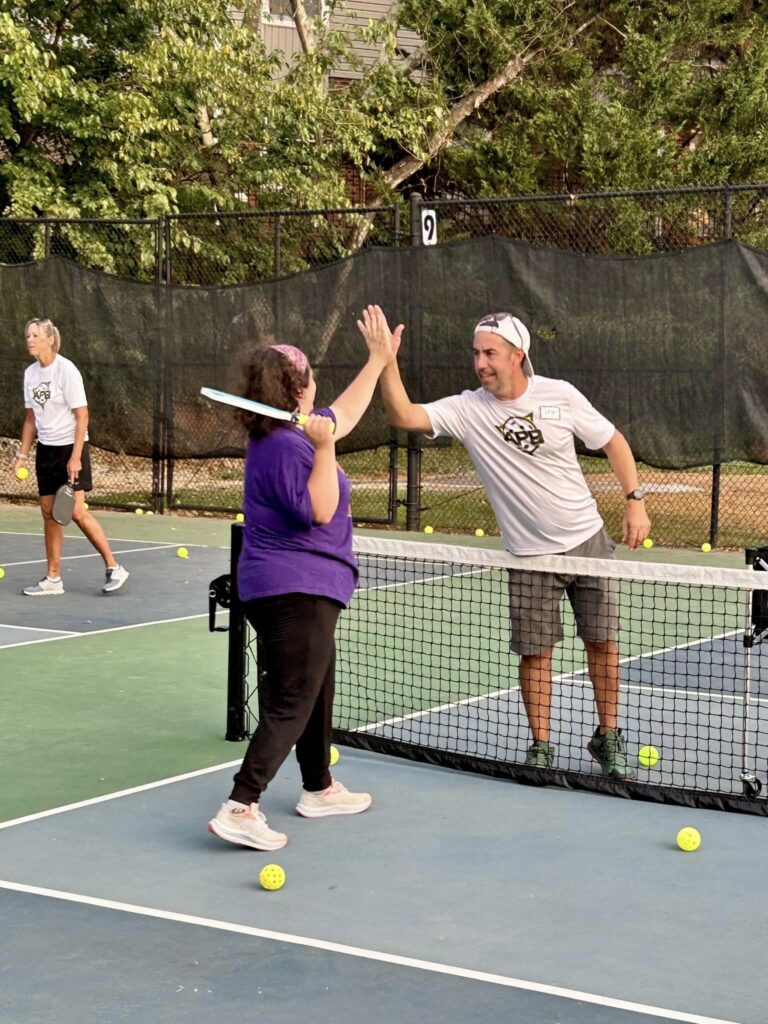 An Adaptive pIckleball staff member gives a young female participant with a purple shirt on a high five.