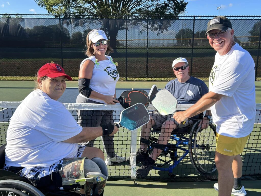 Four people pose for a photo with their pickleball paddles touching as they stand by the net.