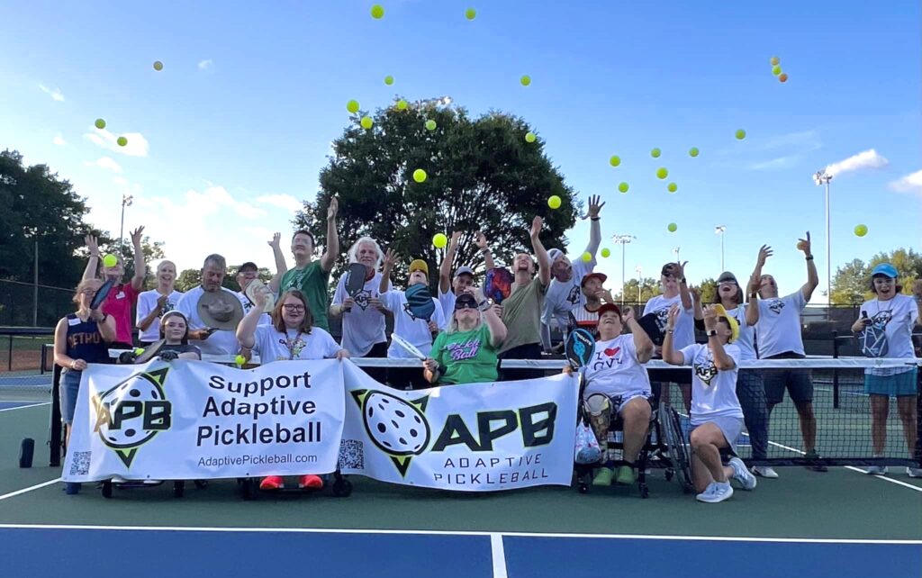 A group of pickleball adaptive athletes throw pickleballs in the air while taking a group photo.